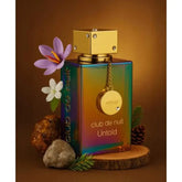 A rainbow-hued 105ml unisex Eau De Parfum by Showlu Well Nation Store, featuring a gold cap and chain, stands among flowers, rocks, pinecones, and greenery—highlighting its long-lasting woody fragrance with deep sensual notes.