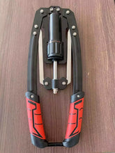 An Adjustable 22-440lbs Hydraulic Power Twister Arm Exerciser with black and red handles and metal arms rests on a wooden surface. This heavy-duty hand-operated device is ideal for chest, shoulder, and wrist muscle training at home.