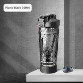 A Premium Electric Protein Shaker Bottle (700ml, piano black), USB rechargeable, stands on a gray surface beside two blueberries, set against a gray concrete background.