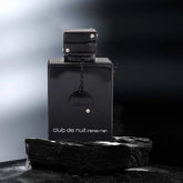 A black bottle of Luxury Men's Fragrance: Night Club Wild Black Edition 105ML by Showlu Well Nation Store sits on a dark stone surface, with a misty gradient background and lighting that highlights its glossy finish.