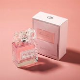 A 50ML Showlu Well Nation Store Eau de Parfum with romantic floral notes—peach, bergamot, rose, and patchouli—in a textured glass bottle with a clear bow cap sits beside its pink and white box on a pink background.
