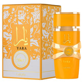 A bright yellow bottle of Lattafa Perfumes Yara Tous for Women Eau de Parfum Spray (3.40 oz/100 ml) by Showlu Well Nation Store stands beside its floral-patterned box, both adorned with gold and white accents and elegant Arabic script.