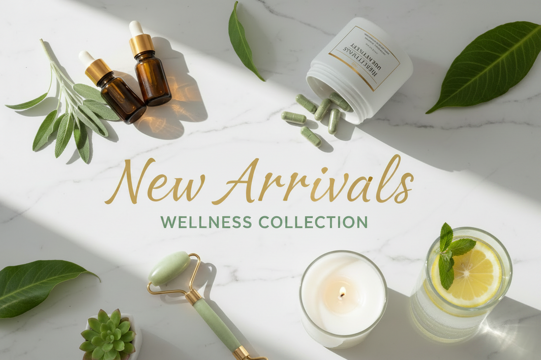 Flat lay of wellness products on a marble surface with greenery, a jade roller, candle, vitamin capsules, dropper bottles, and a glass of lemon water. Text reads: New Arrivals Wellness Collection.