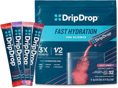A box of DripDrop Hydration Packets Juicy Variety Pack (Grape, Fruit Punch, Strawberry Lemonade, Cherry) is shown with three single-serve electrolyte powder sticks beside it and one being poured into a glass, creating a pink fizz.