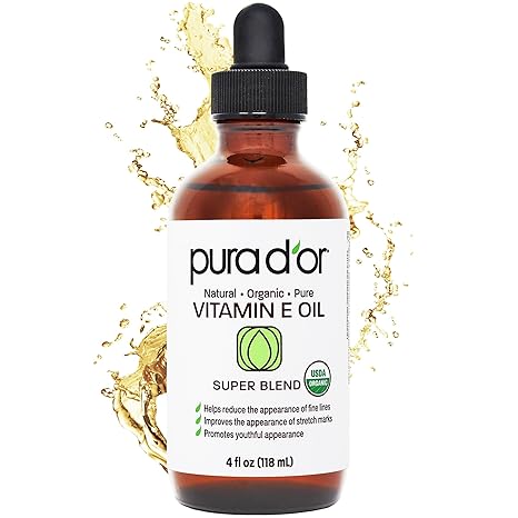 A brown glass dropper bottle of PURA D'OR 4 Oz Organic Vitamin E Oil with a white label is shown before a splash of liquid. This lightweight blend with argan, jojoba, rosehip, apricot, almond, and avocado moisturizes face, body, hair & bath.