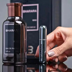 A hand with light-colored nail polish holds a small, metallic Bharara spray next to a larger Bharara King Eau De Parfum 100ml for Men, a citrus fruity cologne with orange, amber, musk, and vanilla notes. The box appears in the background.