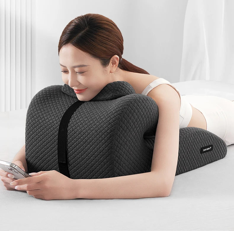 A woman relaxes on her stomach, supported by the New Butt Cushion Multifunctional Prone Position Lie Pillow with unique curved design, using her phone in a bright, minimalistic room.