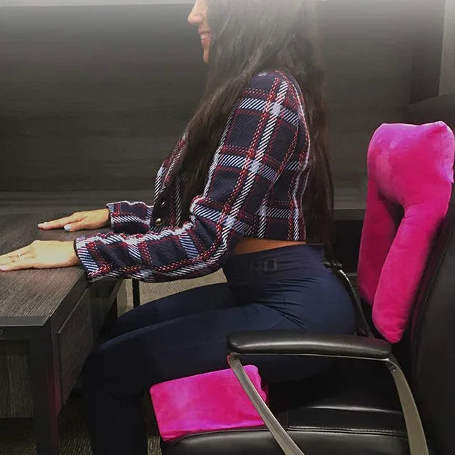 A woman sits at a desk on an office chair using the BBL Pillow Seat Pad, a foam cushion designed for hip surgery rehabilitation and Brazilian Butt Lift recovery, showcasing ergonomic posture with comfort and style in plaid jacket and dark pants.