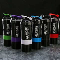 Six 3 Layers Shaker Protein Bottles with black bodies and mixed accent colors—green, purple, white, blue, red, and black—stand on a gray surface against a dark backdrop. Ideal for Mainland China fans seeking quality mixing cups for workouts.