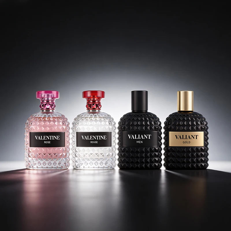 Four 3.4 Fl Oz Eau De Parfum bottles, two clear and two matte black, stand in a row. Featuring Mandarin Orange, Orange Blossom & Bergamot scents, these unisex fragrances are perfect Christmas gifts and shine on the reflective surface.