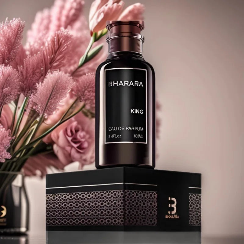 A dark bottle of C2U Bharara King Eau De Parfum 100ML for Men rests on its patterned black gift box, with soft pink flowers in the background, highlighting this high-end 3.4oz spray perfume’s elegant presentation.