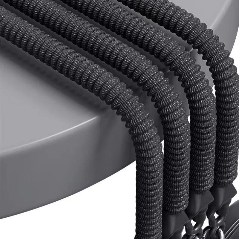 Four black pedal tension ropes from the Pedal Tension Rope Abdominal Strength Elastic Rope are laid over a round gray surface, their metal hooks visible—perfect for home fitness, resistance training, and muscle relaxation routines.