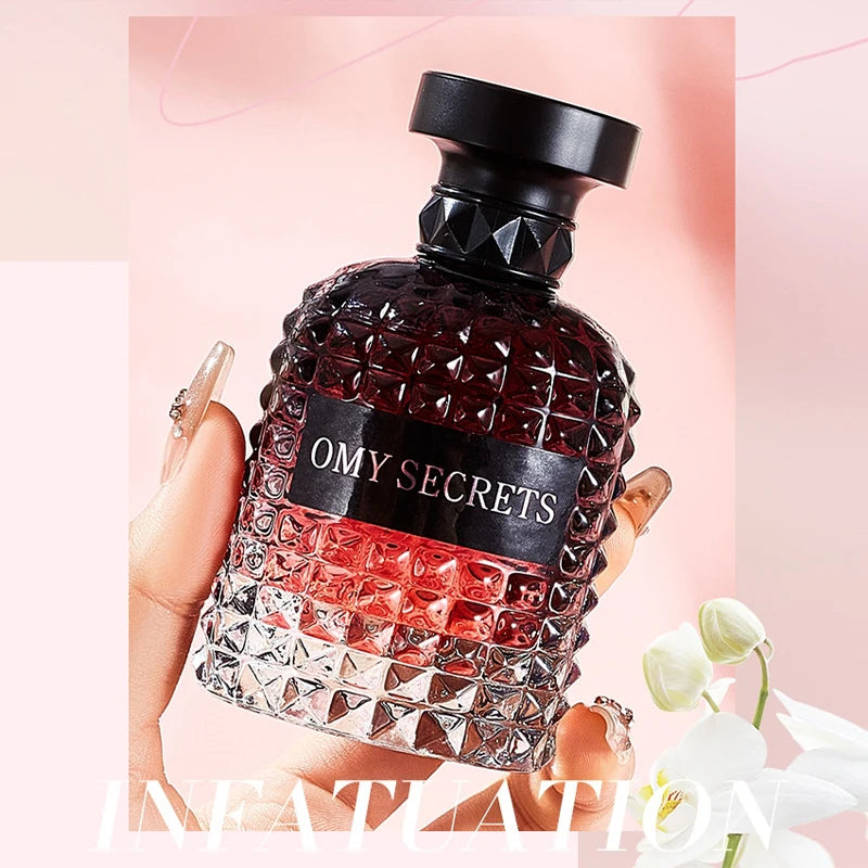 A hand holds a faceted glass bottle of Miss Adventure Donna Perfume against a soft pink background, with white flowers hinting at its floral fruity scent of rose and jasmine, perfect for daytime freshness.