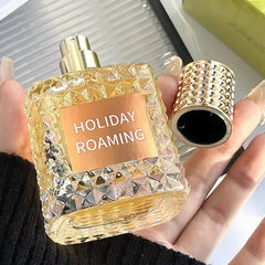 A hand holds the Rivet Series Fresh Perfume, a square bottle of golden liquid with its cap removed. This elegant EDT blends woody, fruity, and floral notes with bergamot for a high-quality, long-lasting fragrance for ladies.