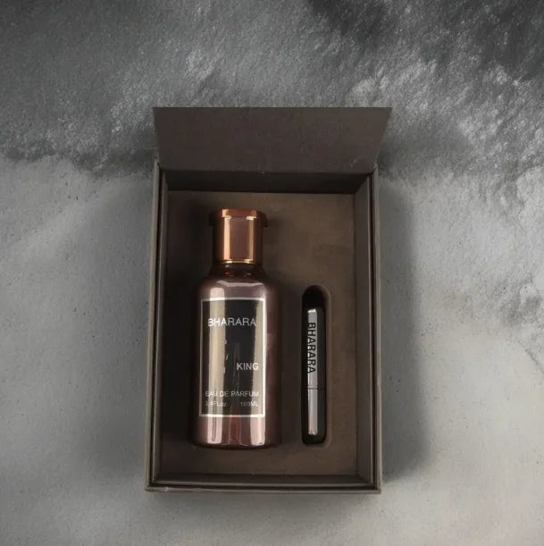 A metallic bottle of Bharara King Eau De Parfum 100ml for men and a small labeled vial sit in a black gift box on a gray textured surface, highlighting the modern luxury of this long-lasting 2025 cologne.