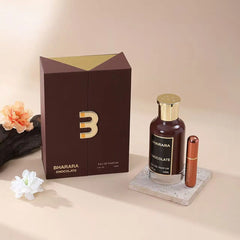 A bottle of Bharara King Men's Eau de Parfum, a rich woody fragrance (100ml), stands on a stone coaster beside its brown and gold box, with a small lipstick and decorative flowers on a neutral background—perfect gift for him.