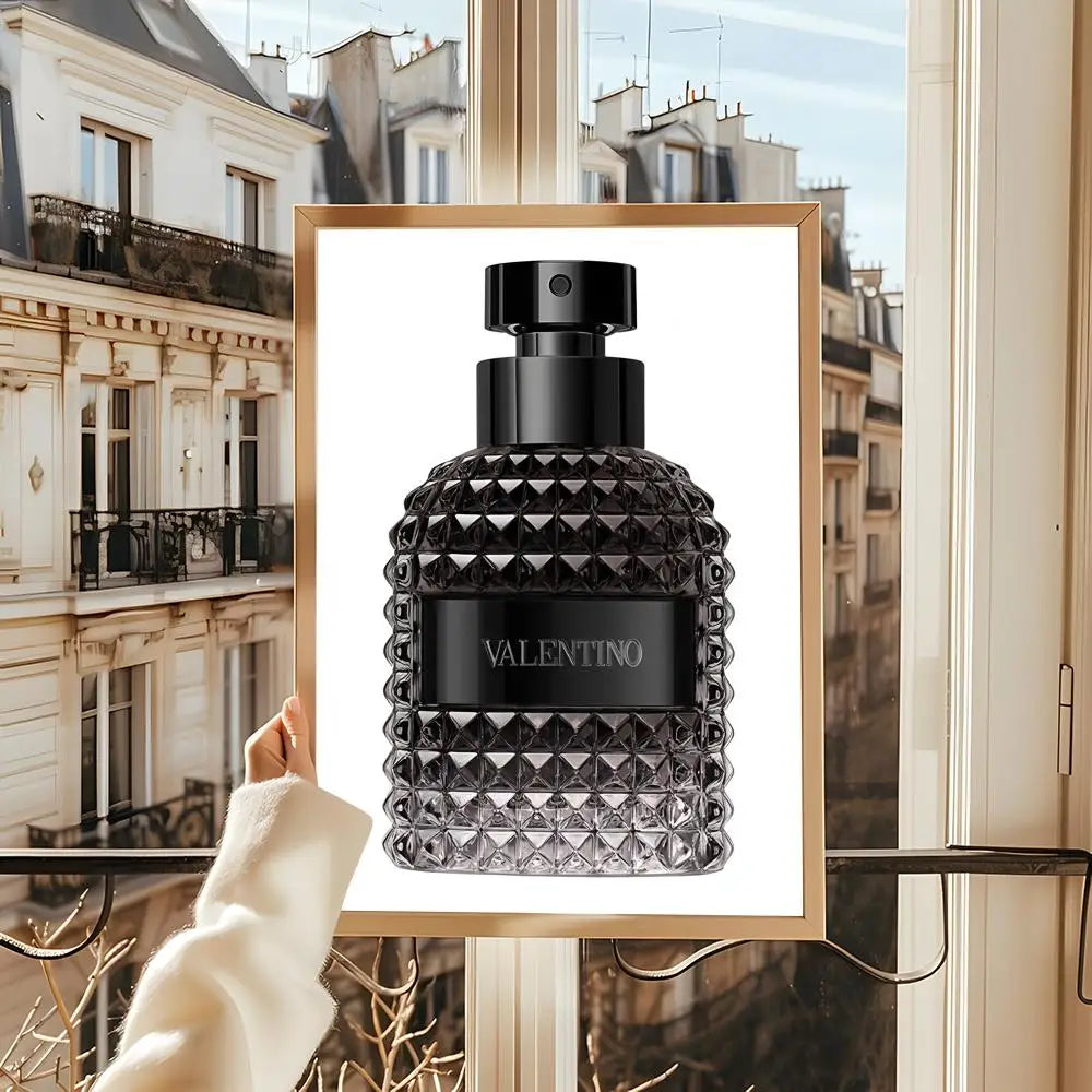 A hand holds a Perfume Bottle Prints Nordic Poster Wall Art, featuring a textured black bottle and classic Parisian buildings through a window—perfect for living rooms, bedrooms, bars, and home decor mural painting decoration.