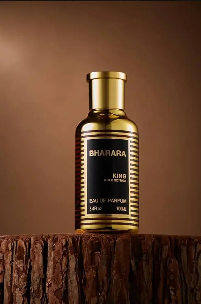 A 100ml bottle of Bharara King Gold Edition Eau de Parfum, inspired by elite gourmand classics, stands upright on a textured tree stump against a brown gradient background.