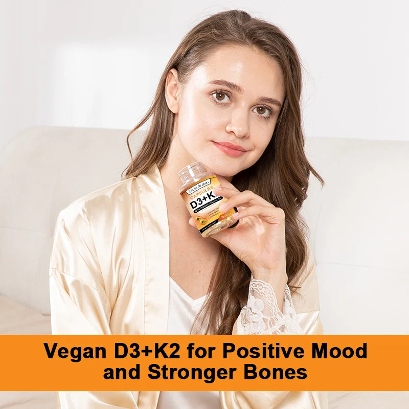A woman in a light robe sits on a couch holding a bottle labeled Vegetarian Vitamin D3K2 Capsules. An orange banner at the bottom reads: Supports Immune System, Heart Health, Strong Bones & Relaxation.
