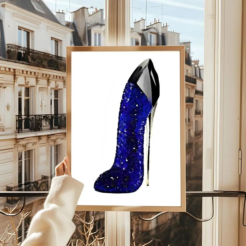 A person holds up the Perfume Bottle Prints Nordic Poster Wall Art, featuring a blue high-heeled shoe-shaped perfume bottle with a black cap, in front of a window overlooking classic Parisian buildings.