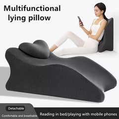 A woman leans against the Lie On The Bed Sleeping Pillow, a large, dark gray multifunctional 100% polyester cushion with a detachable headrest, designed for ergonomic comfort while reading or using her phone.