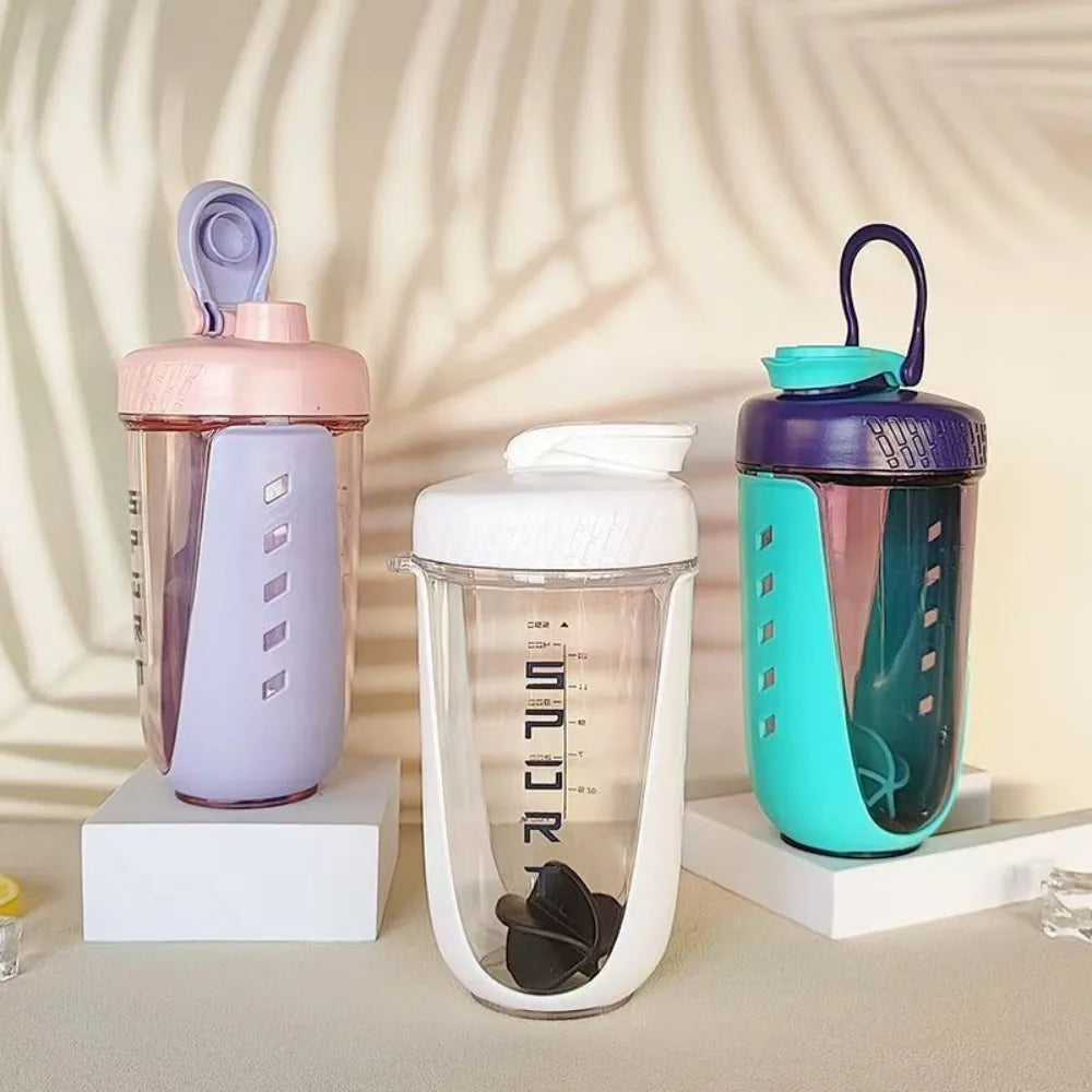 Three Premium Protein Powder Shakers (590ml, BPA-free Tritan) with mixing balls are on white platforms. The pastel purple/pink, white/gray, and teal/navy bottles from China stand before a leaf-shadowed background.